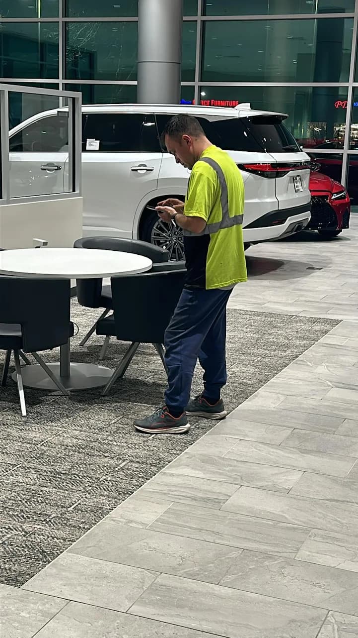 Man in a neon safety vest looks at his phone inside a car dealership.