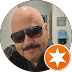 Bald man with a mustache wearing dark sunglasses, featuring an orange star icon badge.