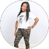 Smiling woman in a white graphic t-shirt and camouflage pants posing against a white background.